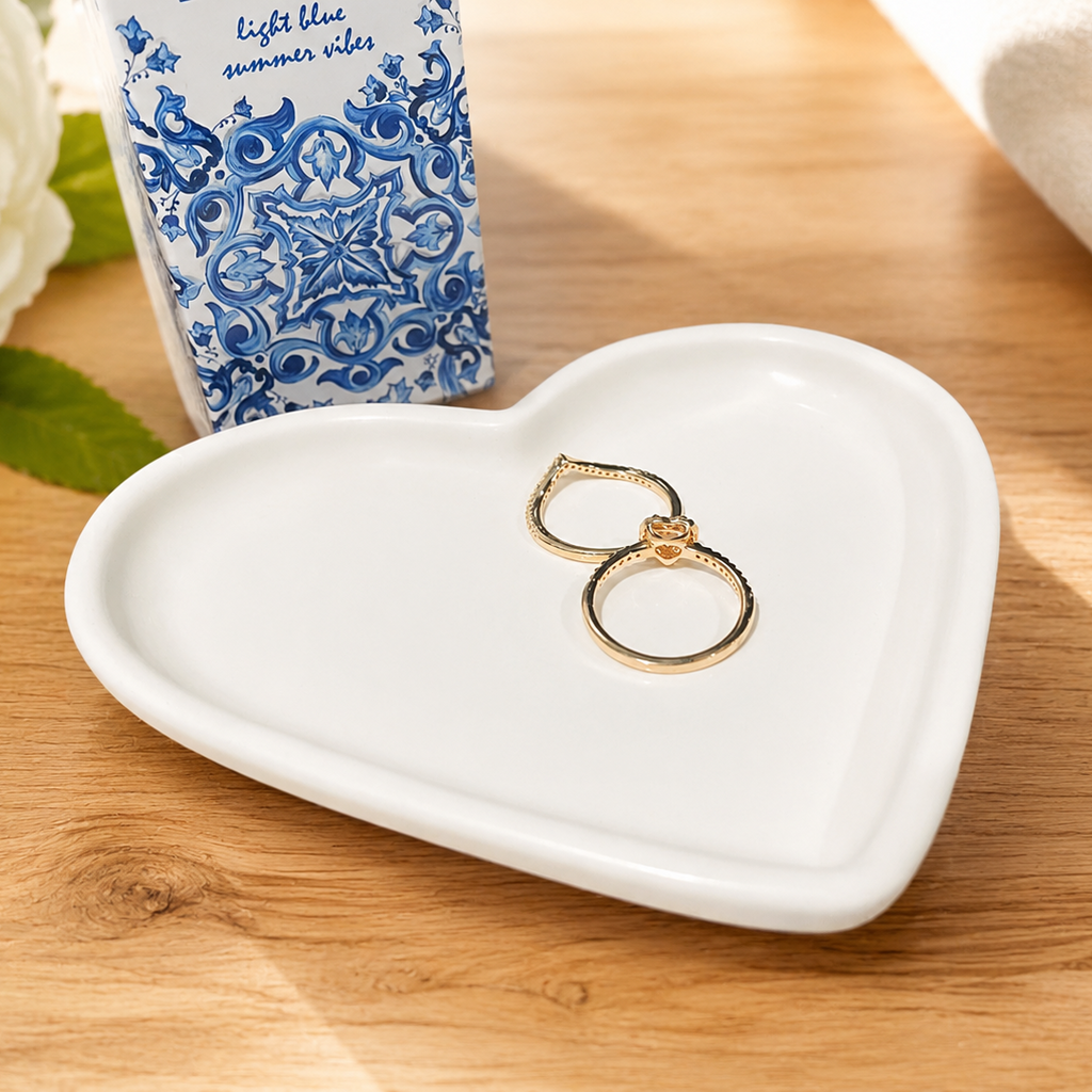 Heart-shaped white jewelry dish with gold rings on a wooden surface with a floral box in the background.